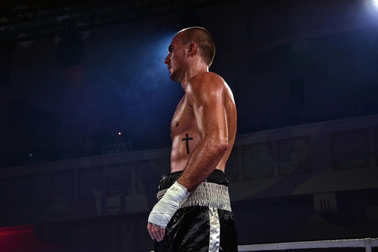 Professional wrestler standing in the ring under spotlight during a live wrestling event