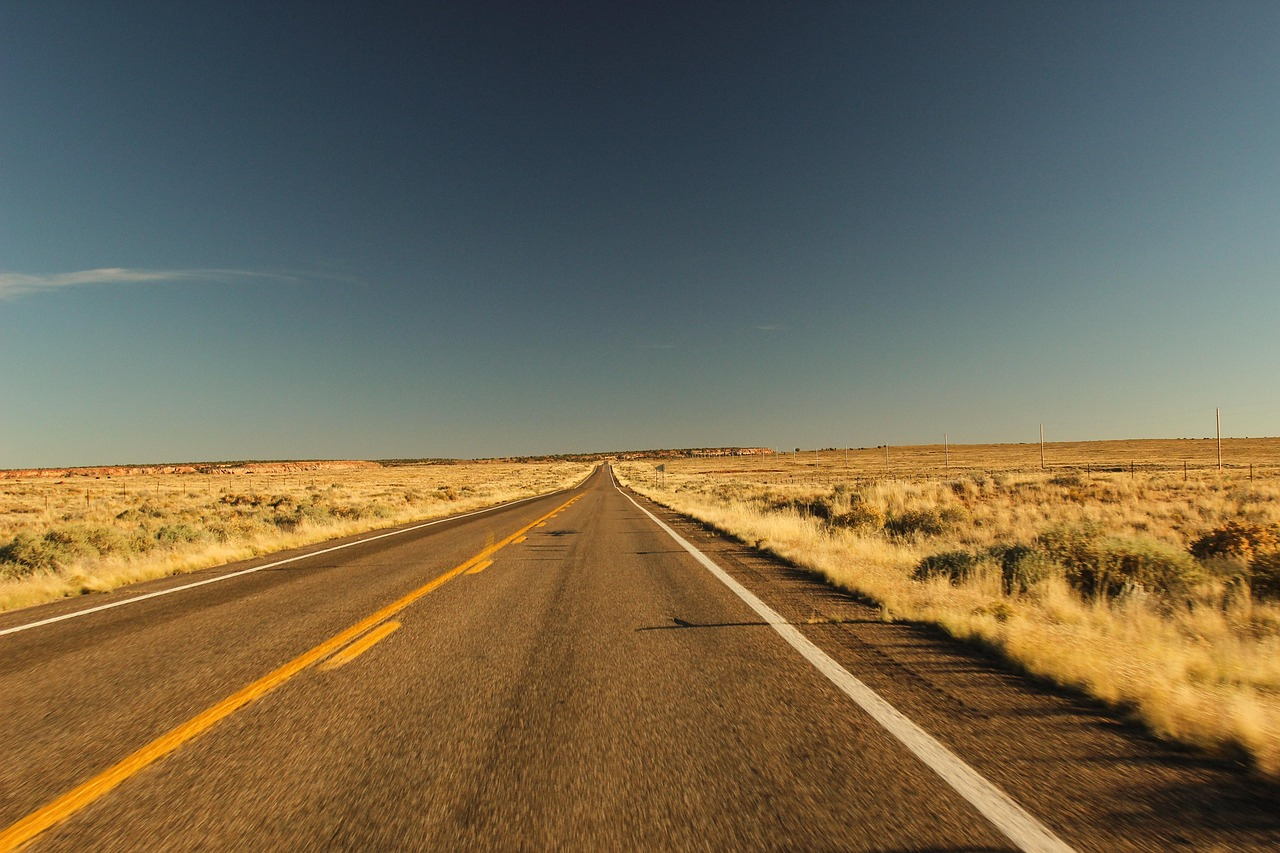 Long straight highway stretching through open dry landscape, symbolising long-distance road trips to major sports events