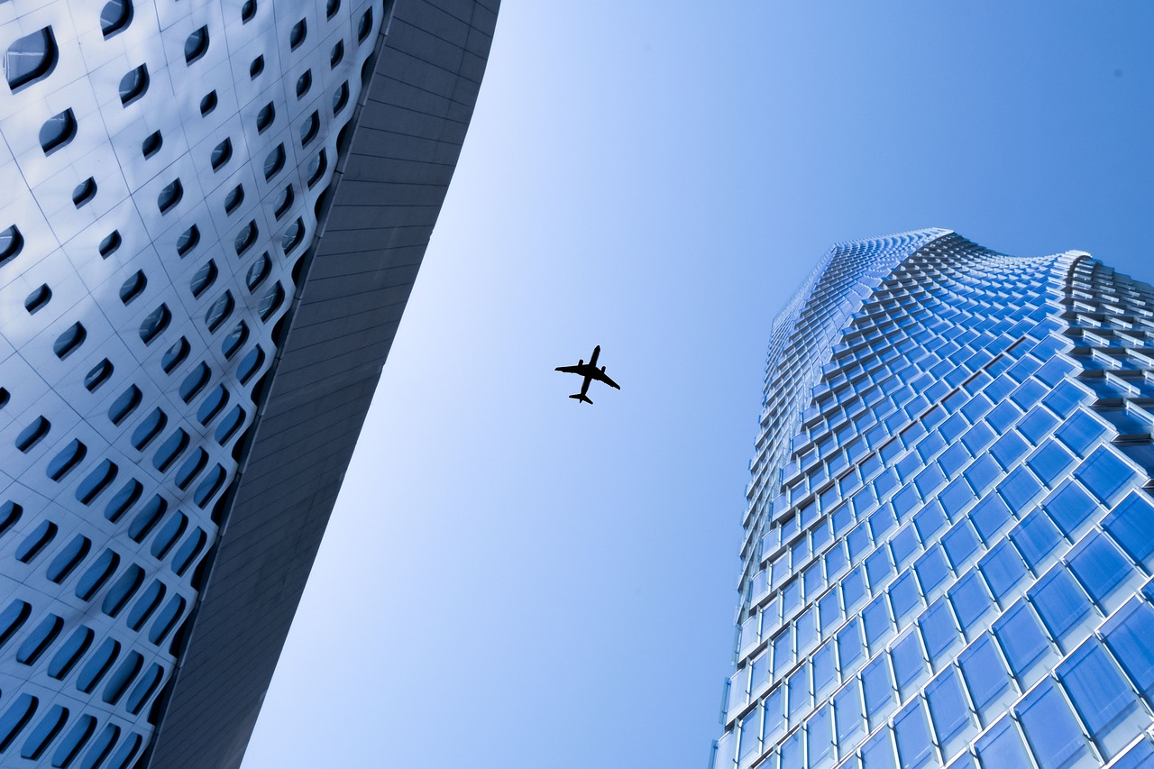 Airplane flying between modern skyscrapers in a major city skyline, symbolizing international travel to major events like WrestleMania